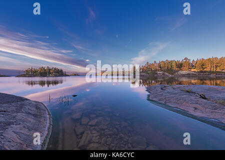 Beautiful sunrise at uninhabited skerries of Ladoga lake, located in Karelia, north of Russia. The rocky lake bed can be clearly seen through quiet an Stock Photo