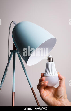 Changing the bulb for led bulb in table lamp in turquoise colours. Stock Photo