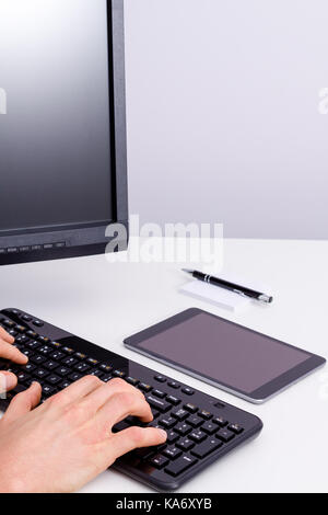 Male hand writing on pc keyboard with laying tablet on desk. Stock Photo