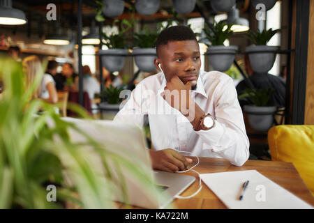 African man thinking, di ided problem, working with laptop at cafe. Stock Photo