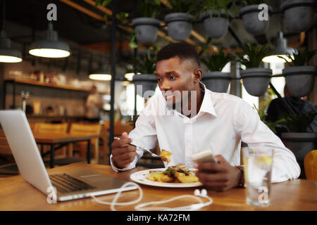 African man having dinner at worjing with laptop in cafe. Stock Photo