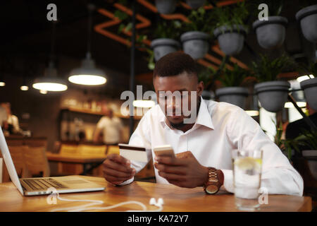 African man pay with card in cafe using call phone. Stock Photo