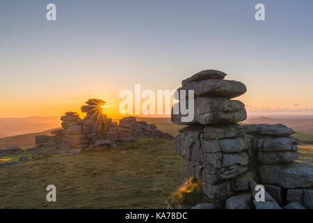 Sunset as the sun dips behind the granite outcrop with starburst effect at Great Staple Tor, Dartmoor National Park, Devon, UK in September Stock Photo