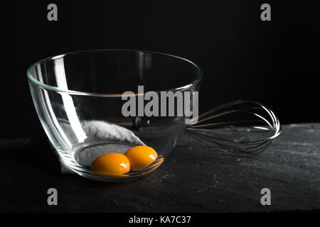 Chicken yolks in a bowl and whisk for beating on a gray table horizontal Stock Photo