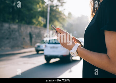 Cropped image of a mobile phone in female hands against a summer city background and road traffic Stock Photo