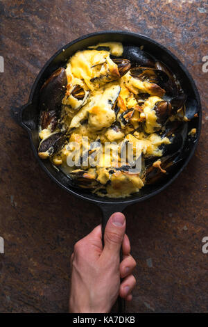 Hand holding a frying pan with mussels on a brown background vertical Stock Photo