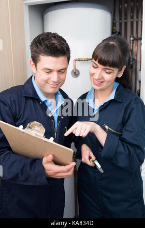 Female Trainee Plumber Working On Central Heating Boiler With Male Engineer Stock Photo