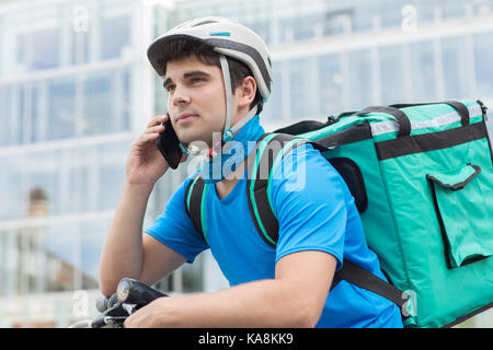 Courier On Bicycle Delivering Food In City Using Mobile Phone Stock Photo