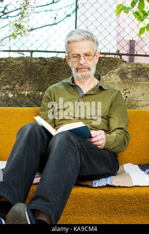 Senior man reading a book on a bed in the backyard Stock Photo