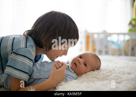 Beautiful boy, hugging with tenderness and care his newborn baby brother at home. Family love happiness concept