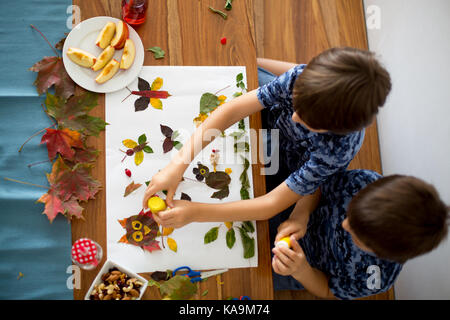 Sweet children, boys, applying leaves using glue while doing arts and crafts in school, autumn time Stock Photo
