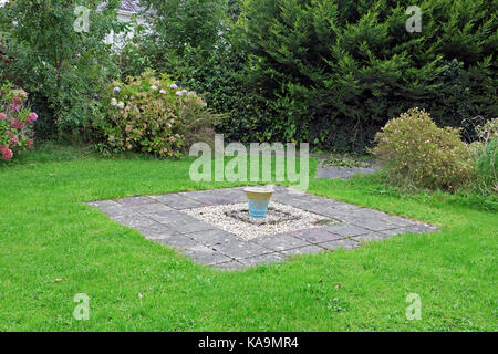 Weeds growing in a single blue ceramic garden pot carefully placed in the centre of a green patch of lawn with gravel & paving slabs UK  KATHY DEWITT Stock Photo