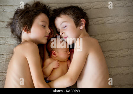 Two children, toddler and his big brother, hugging and kissing their newborn baby brother at home, few days after delivery Stock Photo