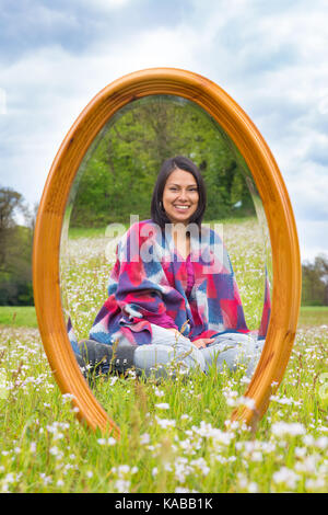 Mirror in blooming spring pasture with sitting pretty colombian woman Stock Photo