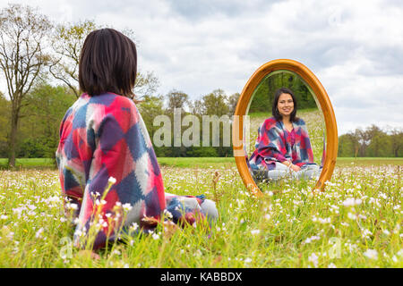 Young colombian woman sitting with mirror in flowering pasture Stock Photo