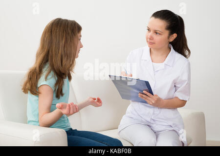 Female Doctor Writing On Clipboard With Patient Sitting On Sofa Stock Photo