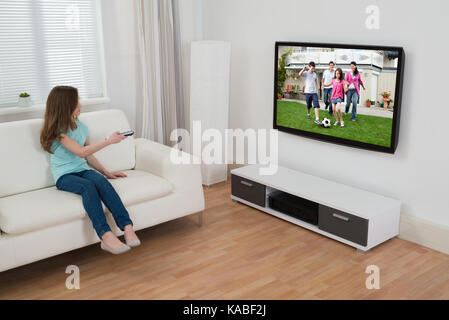 Girl Sitting On Sofa Watching Television In House Stock Photo