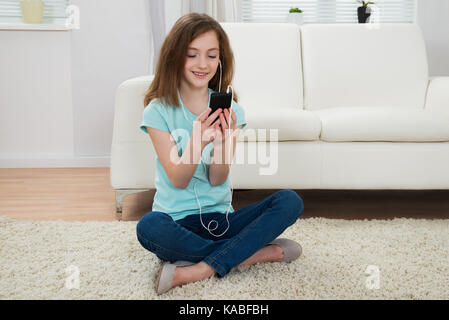 Happy Girl Sitting On Carpet Listening To Music On Mobile Phone Stock Photo