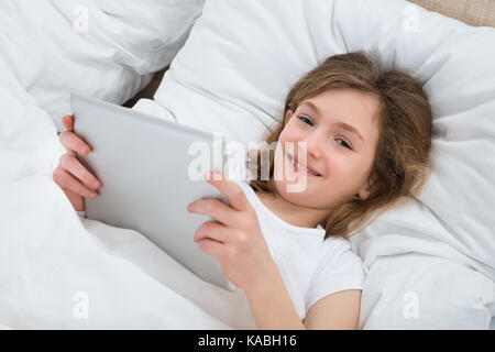 Happy Girl With Digital Tablet Lying On Bed Stock Photo