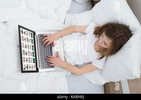 Girl On White Bed Looking At Photos On Laptop In Bedroom Stock Photo