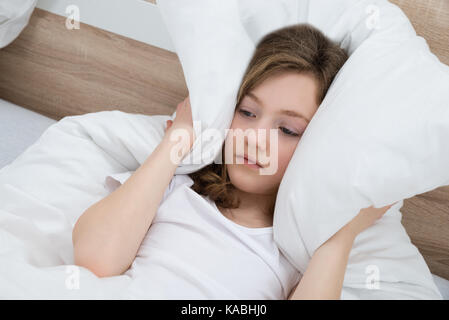 Girl On Bed Covering Ears With Pillow In Bedroom Stock Photo