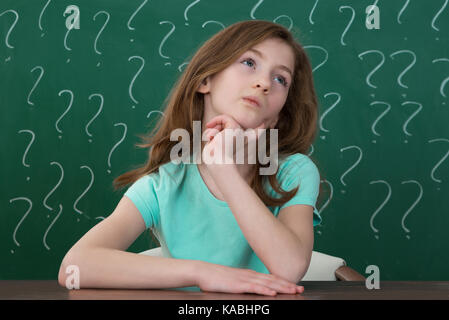 Contemplating Girl Sitting At Desk With Question Mark Drawn In Chalk On The Chalkboard Stock Photo