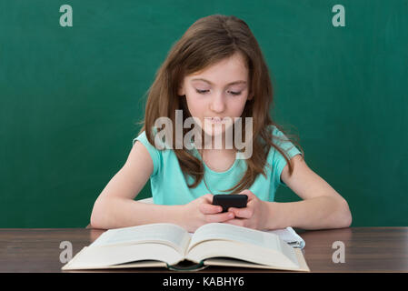 Girl Using Mobile Phone While Studying In Classroom Stock Photo