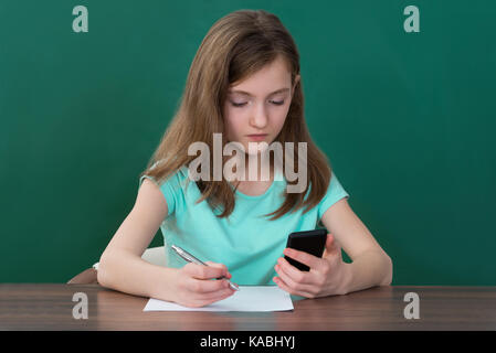 Girl Using Mobile Phone While Studying In Classroom Stock Photo