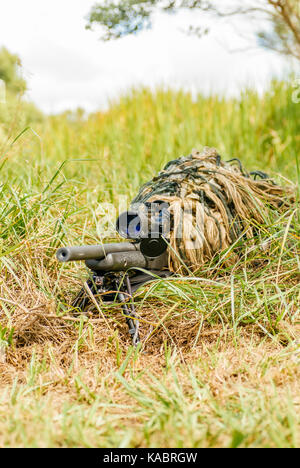 Police SWAT sniper in a ghillie suit looking through a rifle scope surrounded by dense vegetation during a police training exercise in the USA. Stock Photo