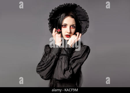 Portrait of brunette woman in black dress and classic gothic style with red eyes on gray background. halloween concept. Stock Photo