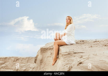 Woman sits on the dunes and dreams of staring into the distance. Stock Photo