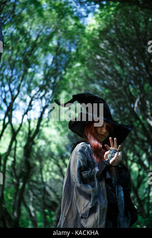 Young witch with long hair with magic ball in hands, long black hat at dark forest Stock Photo