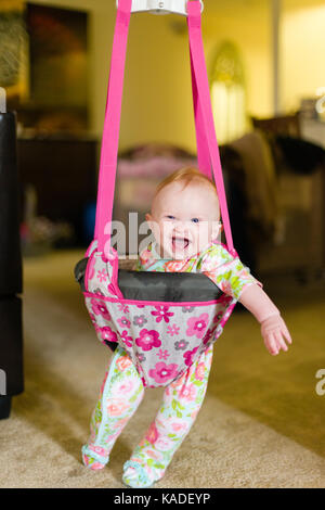 Six month old baby girl in baby bouncer laughing and having fun Stock Photo