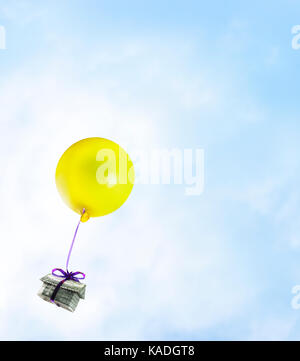Real estate bubble. Origami cash home with yellow balloon on a blue sky. Stock Photo