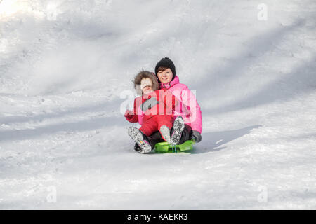 Happy mother and her daughter enjoying a sledge ride down the hills, winter games and fun.  Family holiday and togetherness. Stock Photo