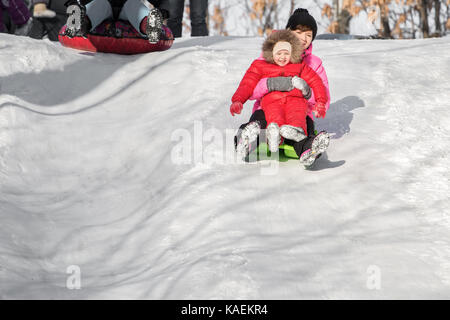 Happy mother and her daughter enjoying a sledge ride down the hills, winter games and fun.  Family holiday and togetherness. Stock Photo