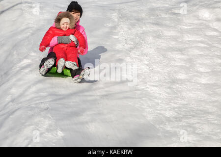 Happy mother and her daughter enjoying a sledge ride down the hills, winter games and fun.  Family holiday and togetherness. Stock Photo