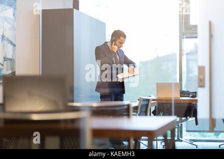 Businessman talking on mobile phone while looking at wristwatch. Stock Photo