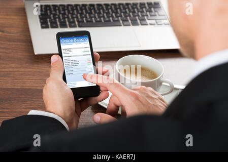 Close-up Of A Businessman Using Online Banking Service On Cellphone While Having Coffee Stock Photo
