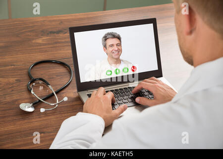 Close-up Of Doctor Talking To Male Patient Through Video Chat On Laptop At Desk Stock Photo