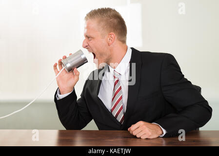 Young Businessman Screaming In Tin Cans Phone At Desk Stock Photo