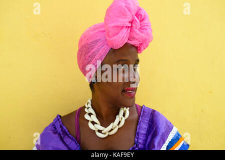 A Cuban woman wears brightly coloured clothes as she sits on the streets of Havana, Cuba. Stock Photo