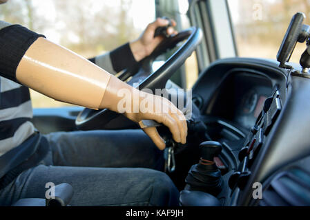Disability, man driving a lorry with a right prosthetic hand and driving pins on the steering wheel for the left hand Stock Photo