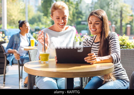 Two joyful women watching video on tablet in cafe Stock Photo