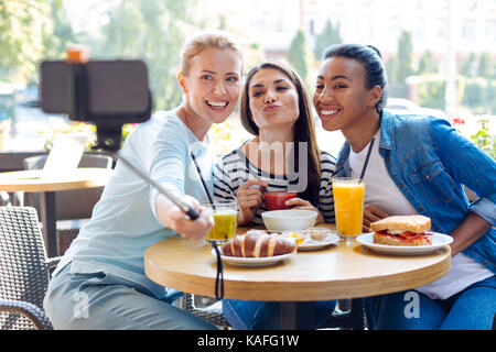Three beautiful women posing while taking selfies in cafe Stock Photo
