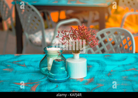 Modern hipster style teal and orange table arrangement in cafe or restaurant - flowers in pot, ashtray and candle Stock Photo