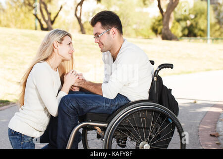 Girl sitting in front of her disabled boyfriend in a wheelchair in the park Stock Photo