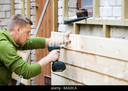 construction worker installing wooden planks on house facade Stock Photo