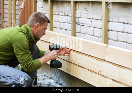 construction worker installing new wooden planks on old house brick facade Stock Photo