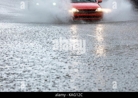 car driving on flooded city road with water spraying from the wheels Stock Photo